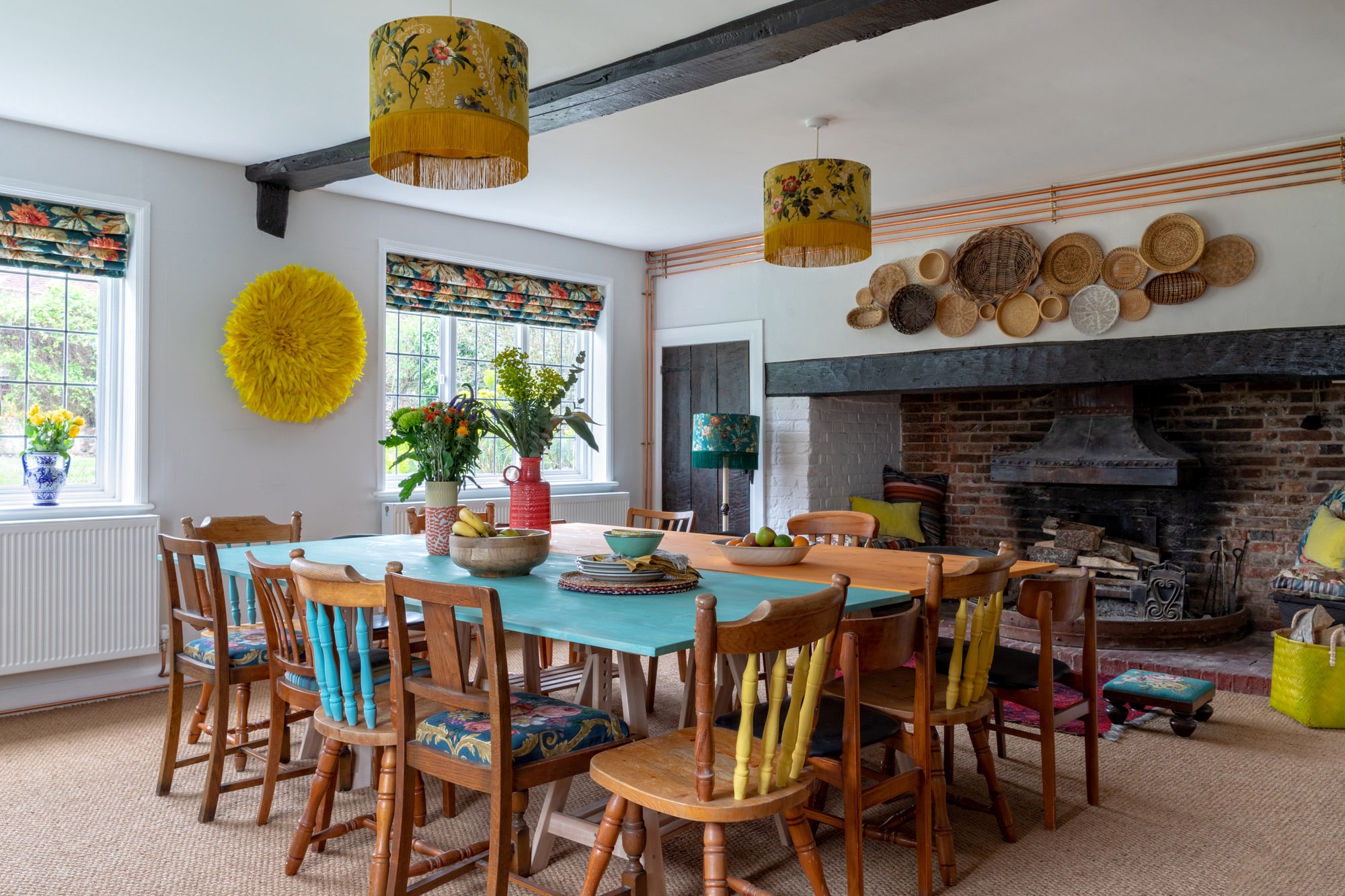 country house photo: colourful dining room, wooden tables, fireplace and woven baskets above it