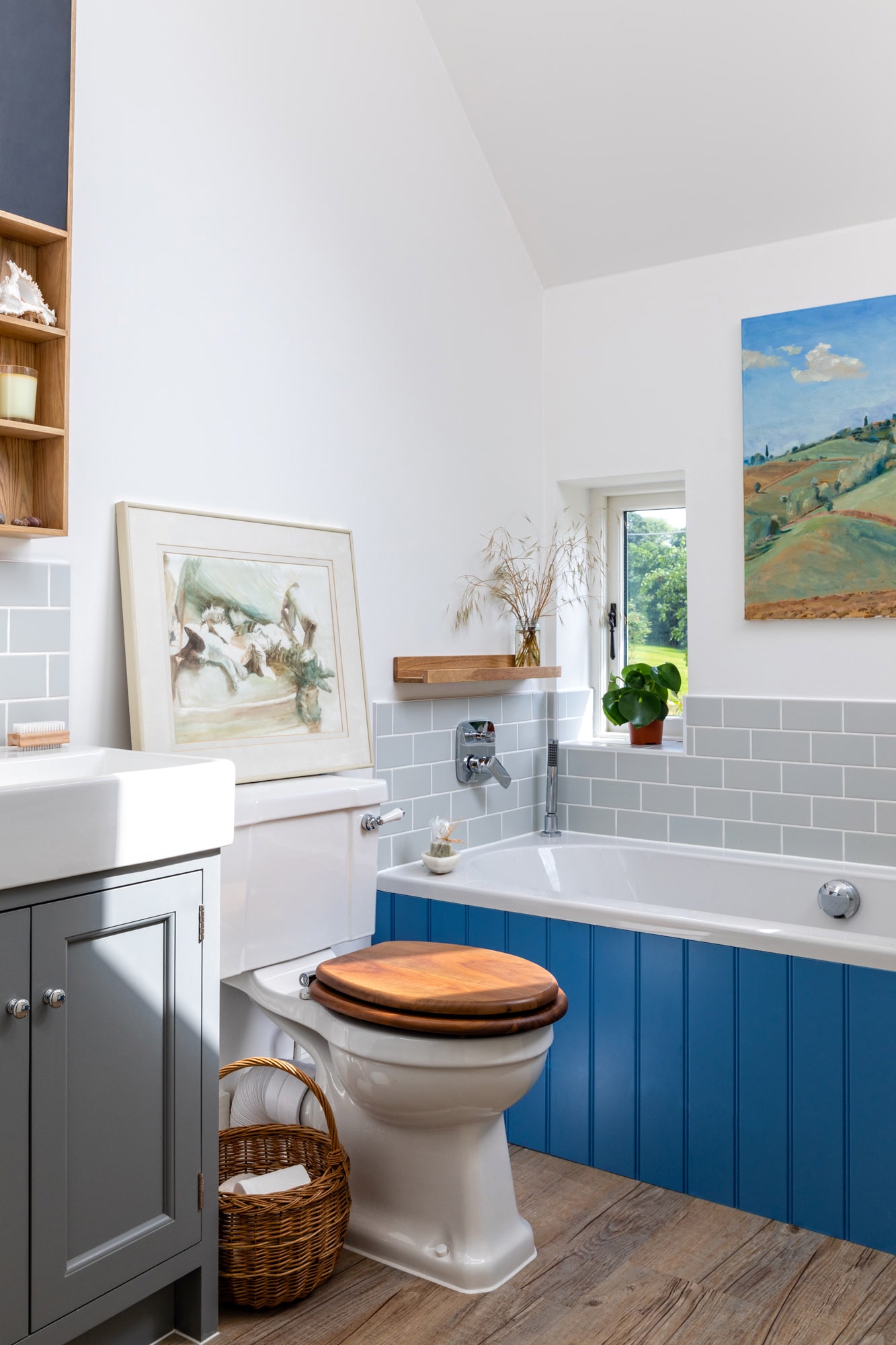 Interior design photography: bathroom in a country house with blue paneling on a bathtub, landscape art on the wall