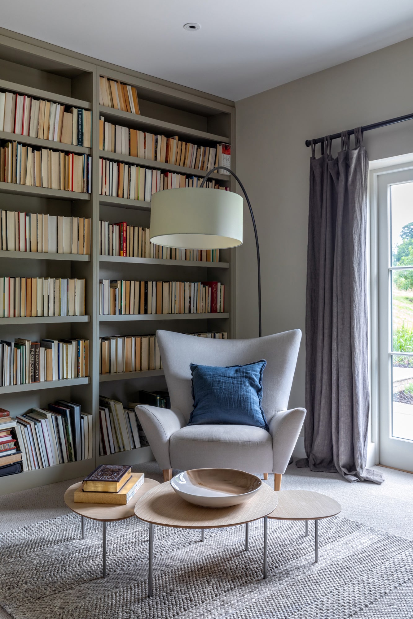Interior photo: library in a country house; shelves with books, a high standing lamp, a grey armchair and a coffee table