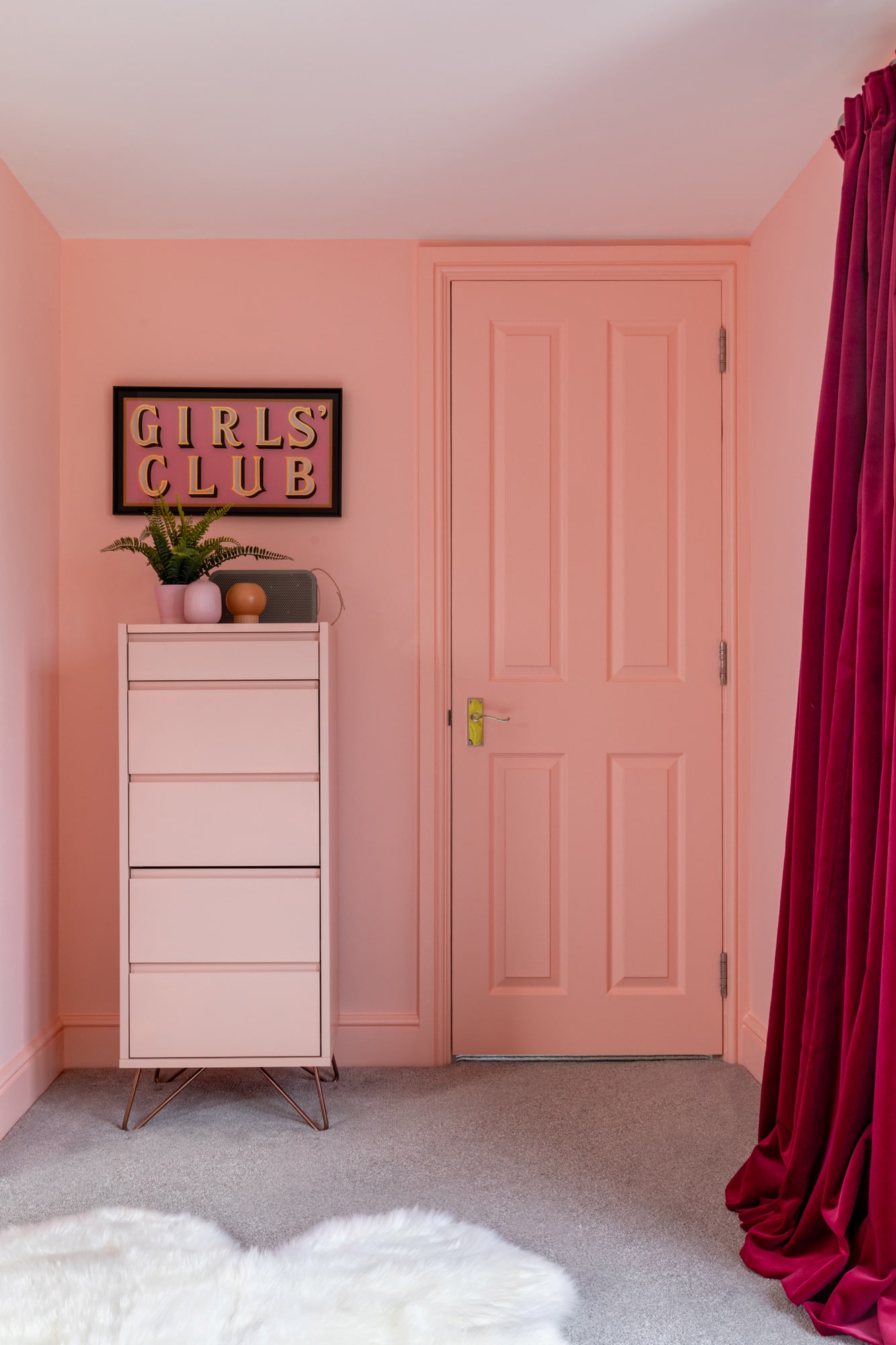 Interior photography: girl's pink bedroom; pink chest of drawers with plants and speaker on top; poster with sign 