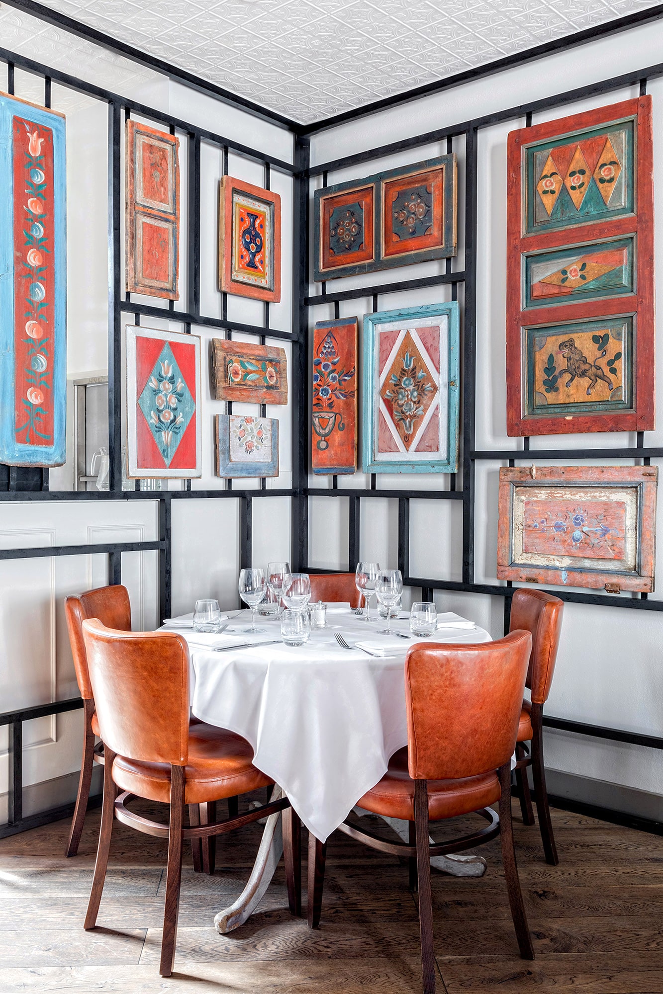 Interior photo of a Russian restaurant: orange leather chairs; tables with white cloths; traditional old Russian decor on the wall; view from the room to the outside patio
