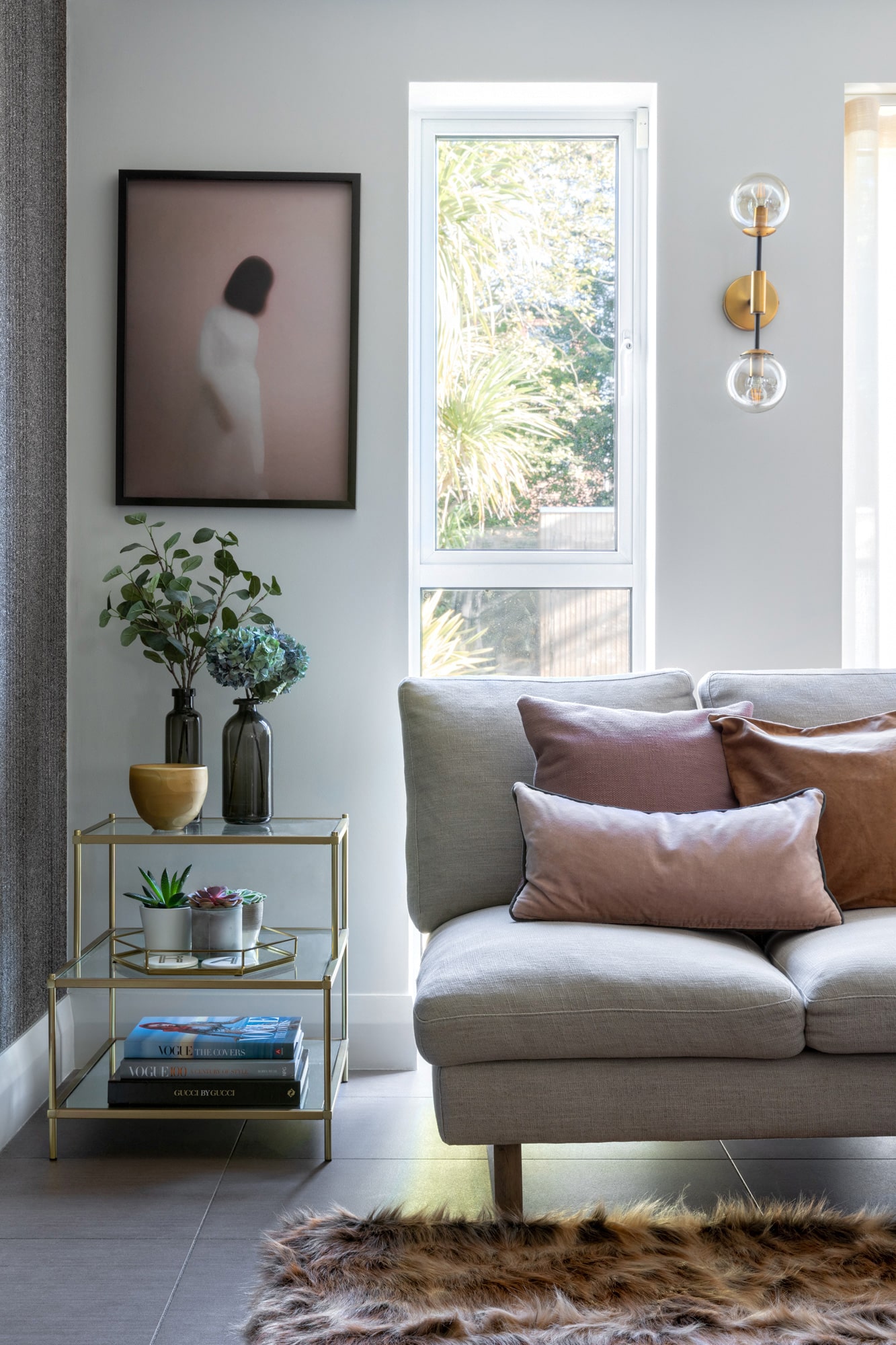 interior photo of a living room: grey feature wall, light grey sofa with pink and grey cushions; glass side table, girl on pink background art