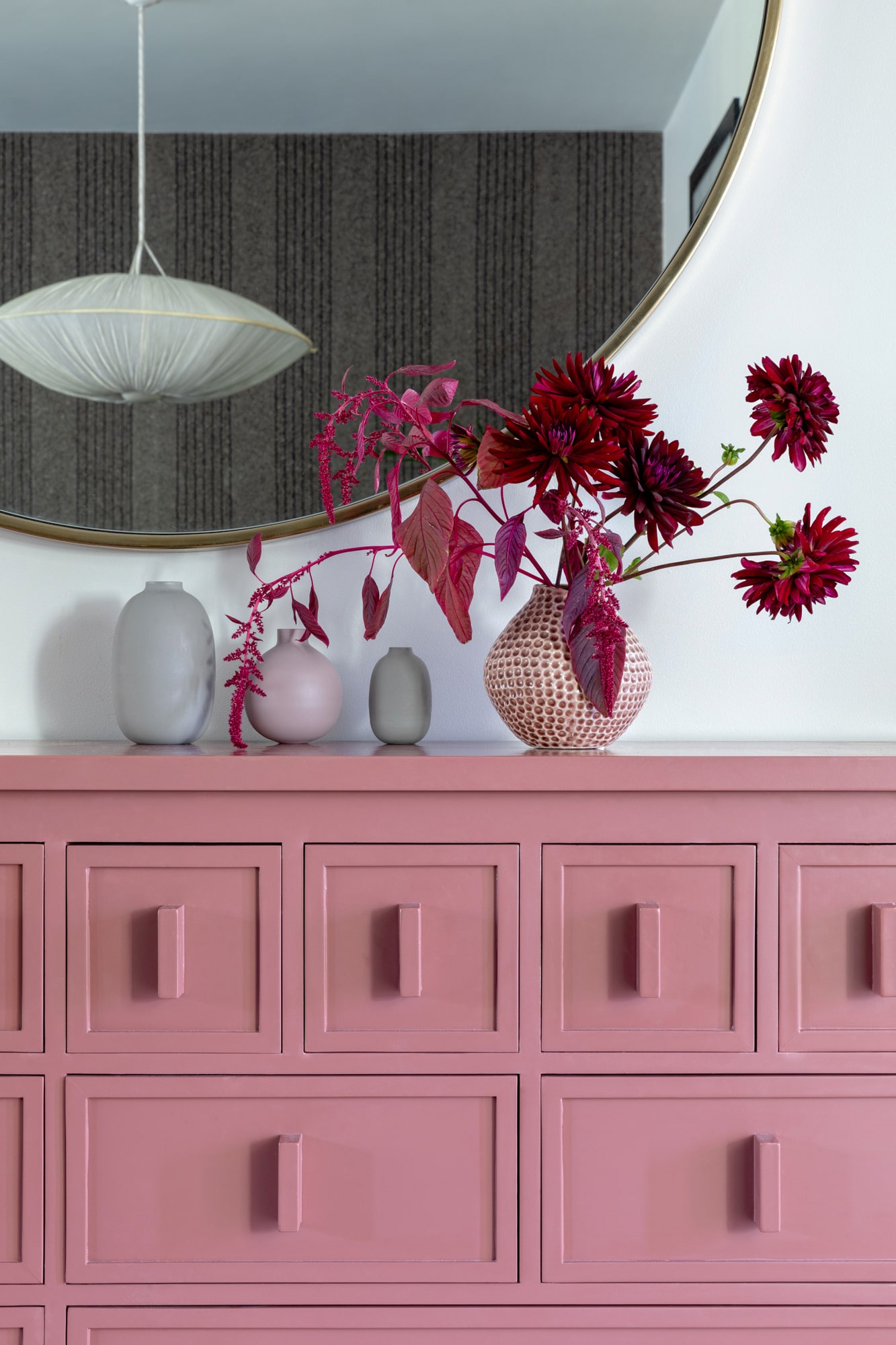 interior detail shot: pink cabinet, burgundy flowers, mirror with a ceiling lamp reflection