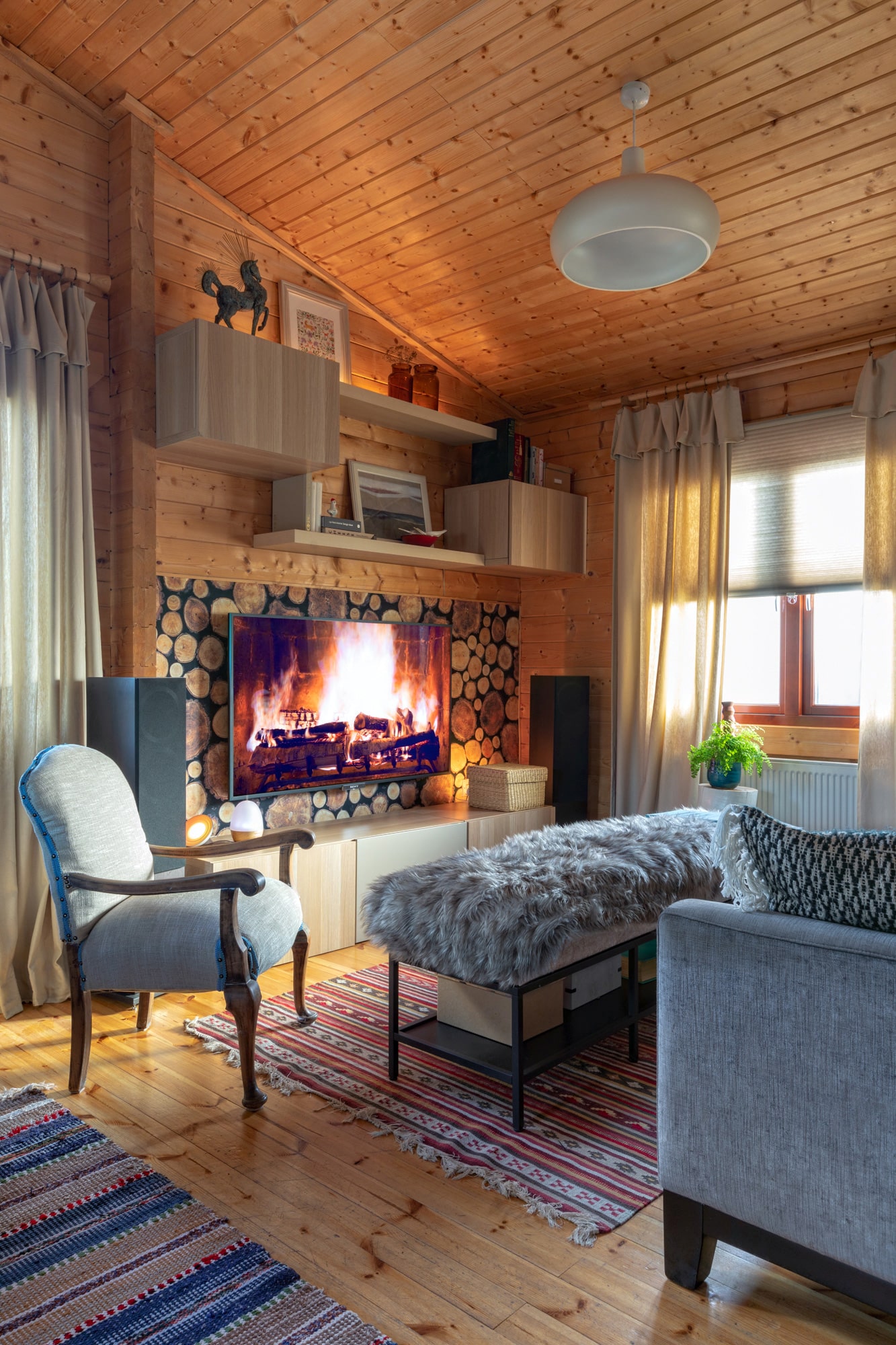 Interior photo of a log cabin: living room; tv with a fireplace lockscreen, a blue sofa, blue armchair