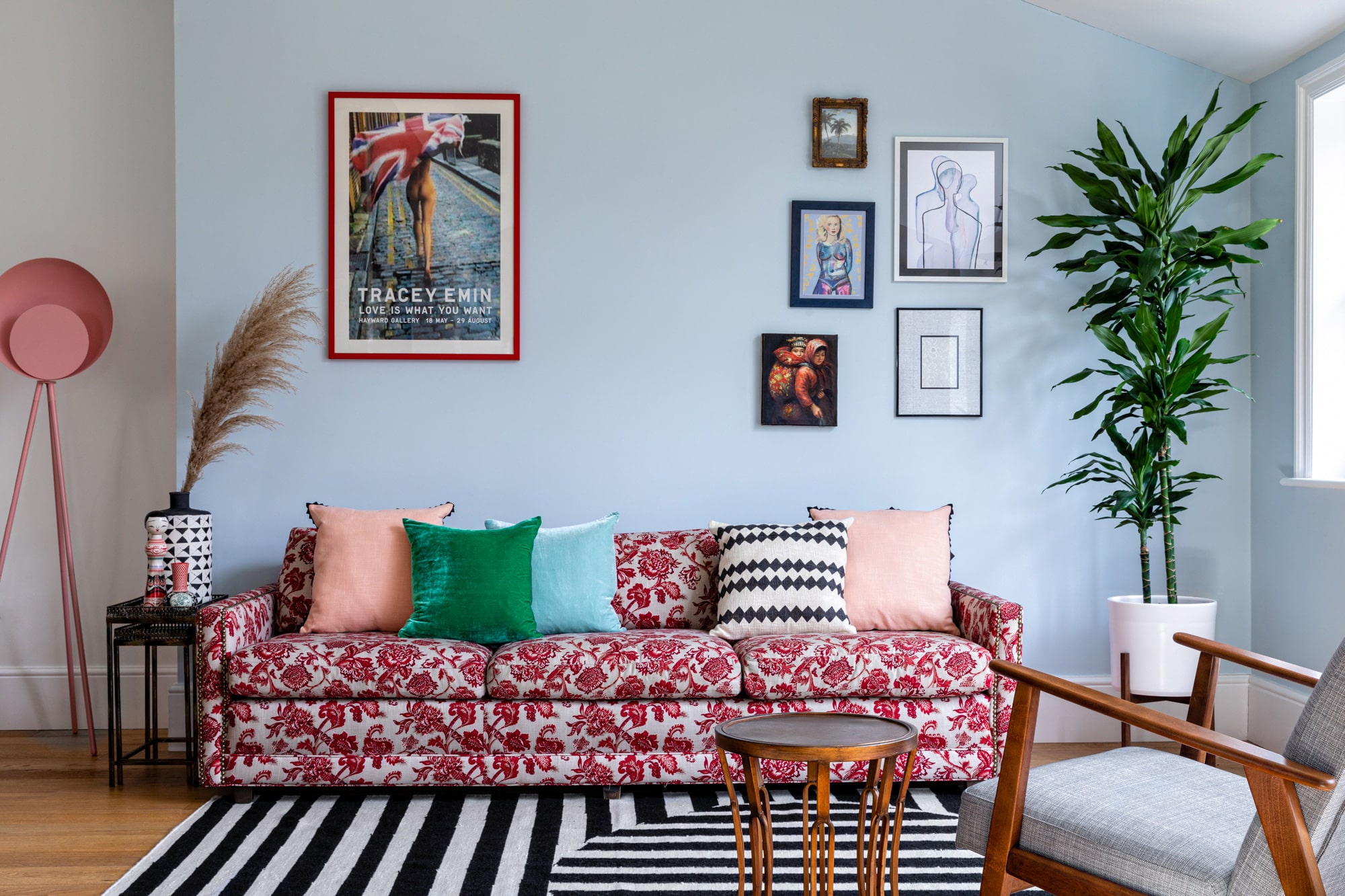 Interior photo of a living room: light blue walls; sofa with red pattern; colourful cushions; Tracey Emin poster; black and white striped rug; wall art gallery