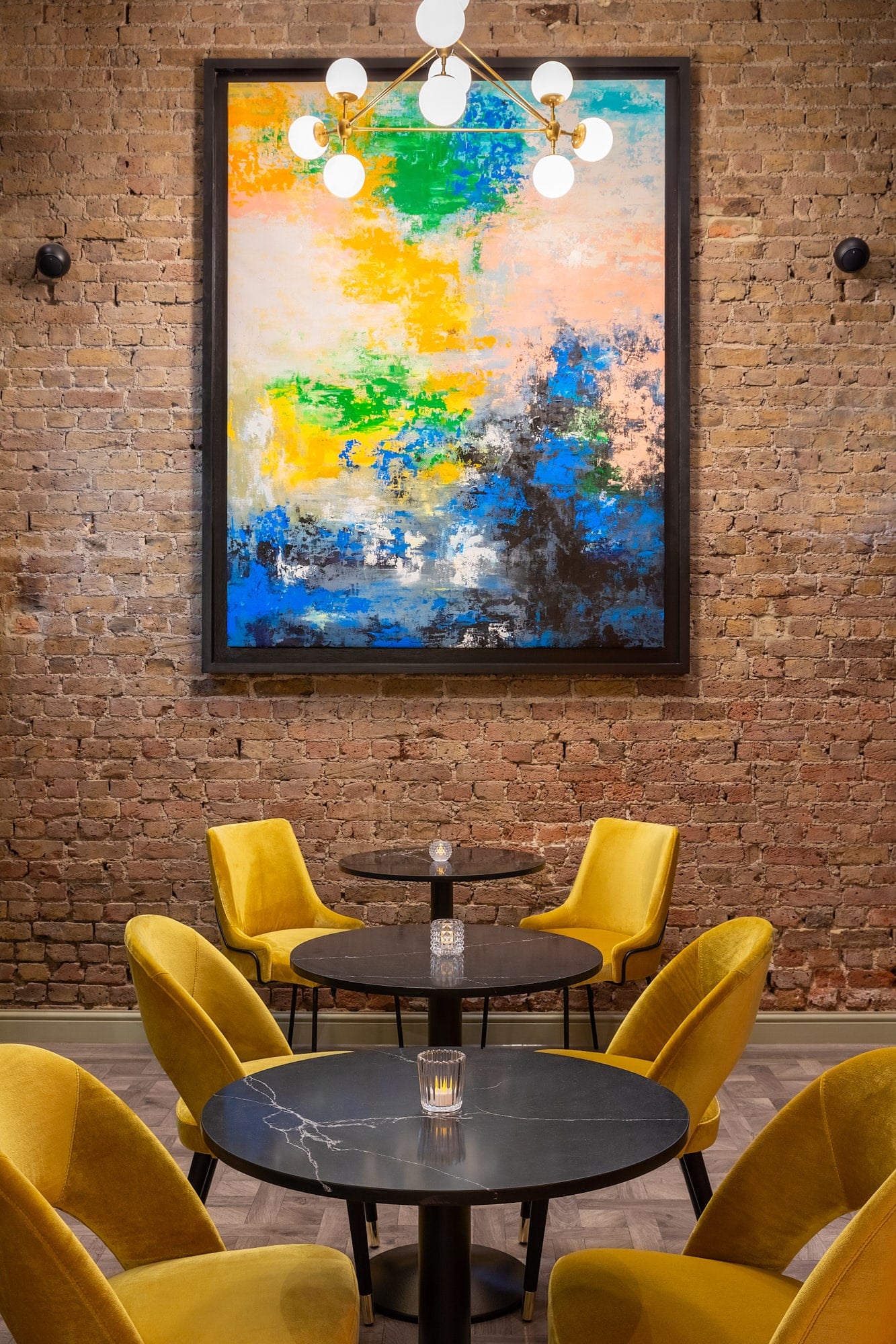 Round tables and yellow velvet chairs with an art on the wall and light
