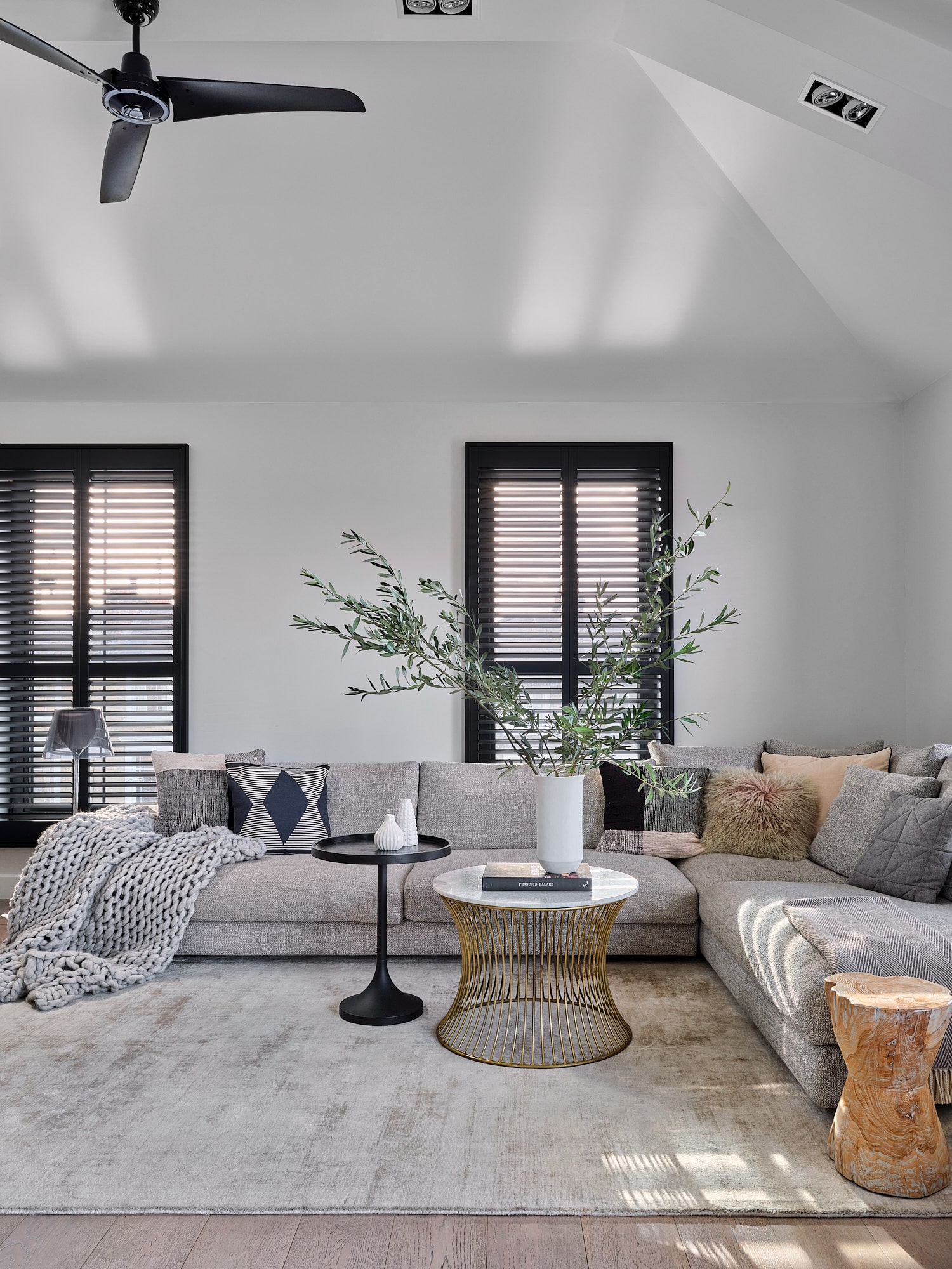 Living room with white walls, black shutters, sofa, two round coffee tables